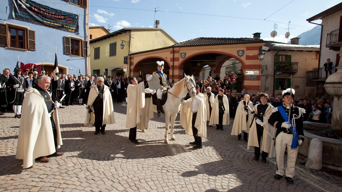 Nella fotografia: Un momento de Le Parlate in cui si vedono i vari personaggi, tra cui El Capitani a cavallo nella piazza del Municipio di Entracque | Arch. Gruppo storico Le Parlate