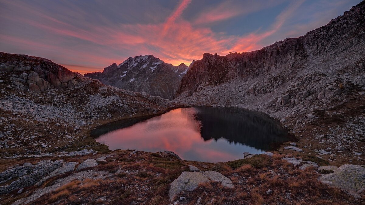 La fotografia di M. Lucotti mostra l'Argentera visto da Fremamorta. La montagna si riflette nel lago, il cielo e le nuvole hanno riflessi rosa. Fine della descrizione.