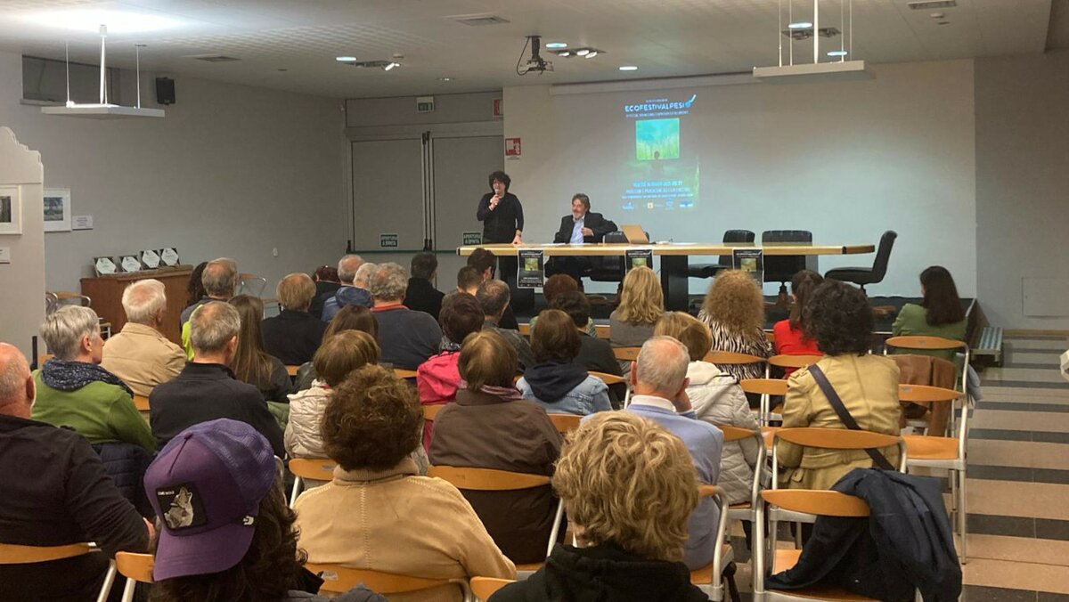 La fotografia mostra un gruppo di persone, riprese di spalle, sedute all'interno della sala incontri R. Mucciarelli a Chiusa Pesio. Di fronte a loro, il proiettore e davanti Erika Chiecchio (a sinistra in piedi) e Giancarlo Baudena, pronti a presentare i film vincitori dell'EcoFestiValPesio. Fine della descrizione.