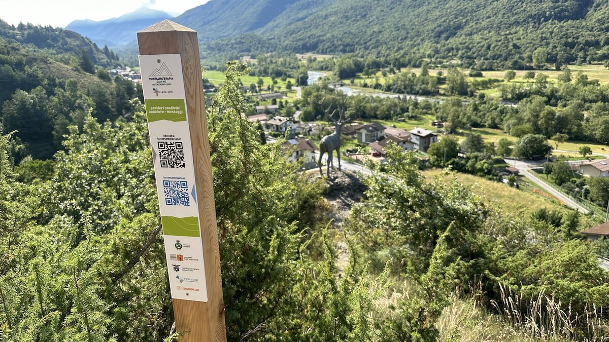 La fotografia di G. Bernardi mostra un palo con il Qr-code, sul sentiero delle Grotte di Aisone, attraverso il quale si rivivono le emozioni del Gruppo di Montagna Terapia dell'Asl Cn1. Fine della descrizione.