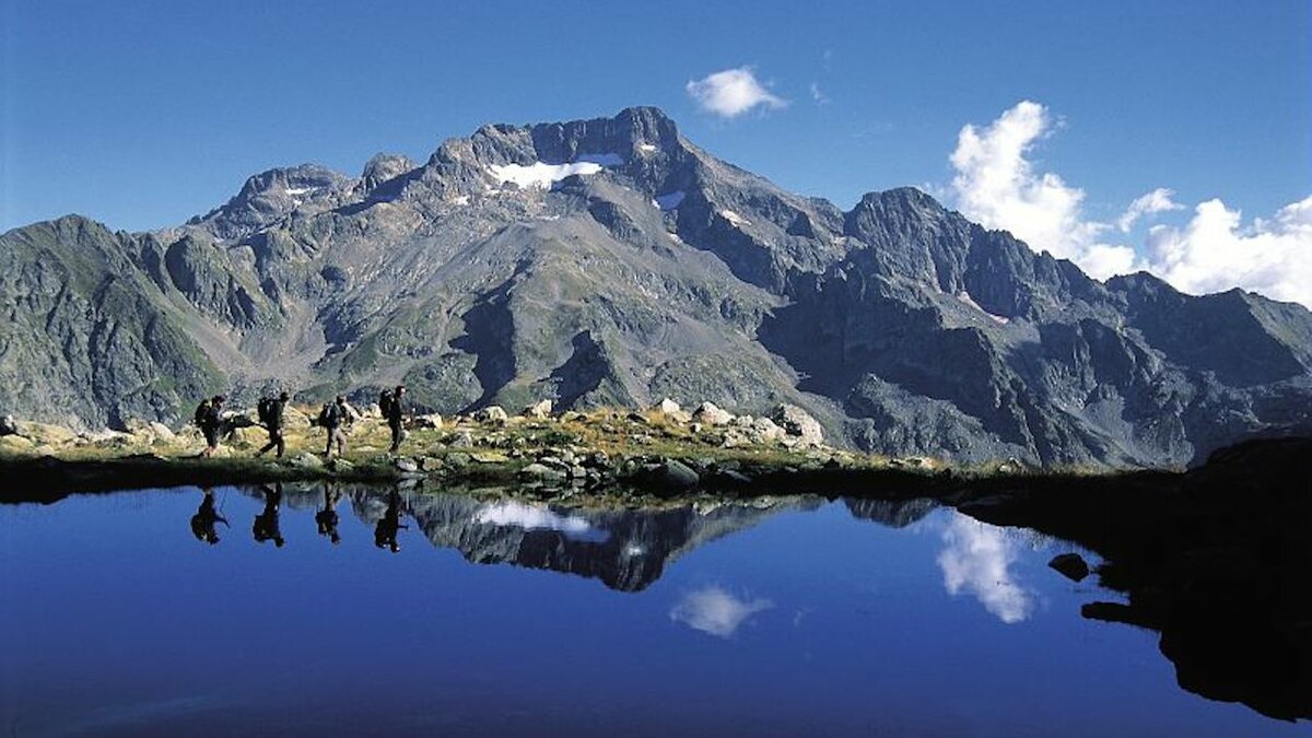 La fotografia di N. Villani mostra un gruppo di escursionisti che cammina sul bordo del lago. Alle loro spalle si vede il Gelas. La fotografia è stata scattata in occasione della traversata del Parco organizzata con il Mercantour per il loro 25° anniversario. Fine della descrizione.