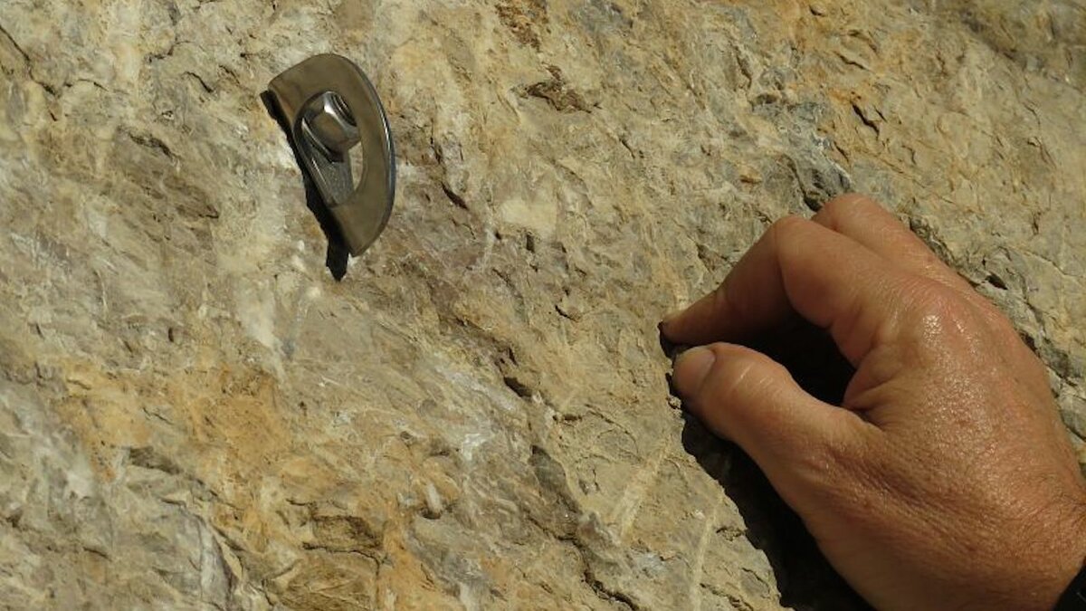 La foto di A. Rivelli mostra la mano di un arrampicatore e, poco sopra, un gancio. Fine della descrizione.