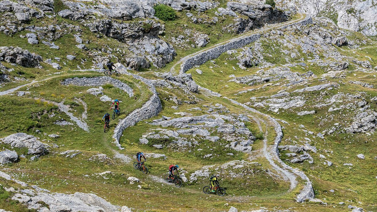 Lo scatto, realizzato da R. Croci per Conitours, mostra alcuni ciclisti che percorrono la discesa sulla Ciclovia del Duca. Fine della descrizione.