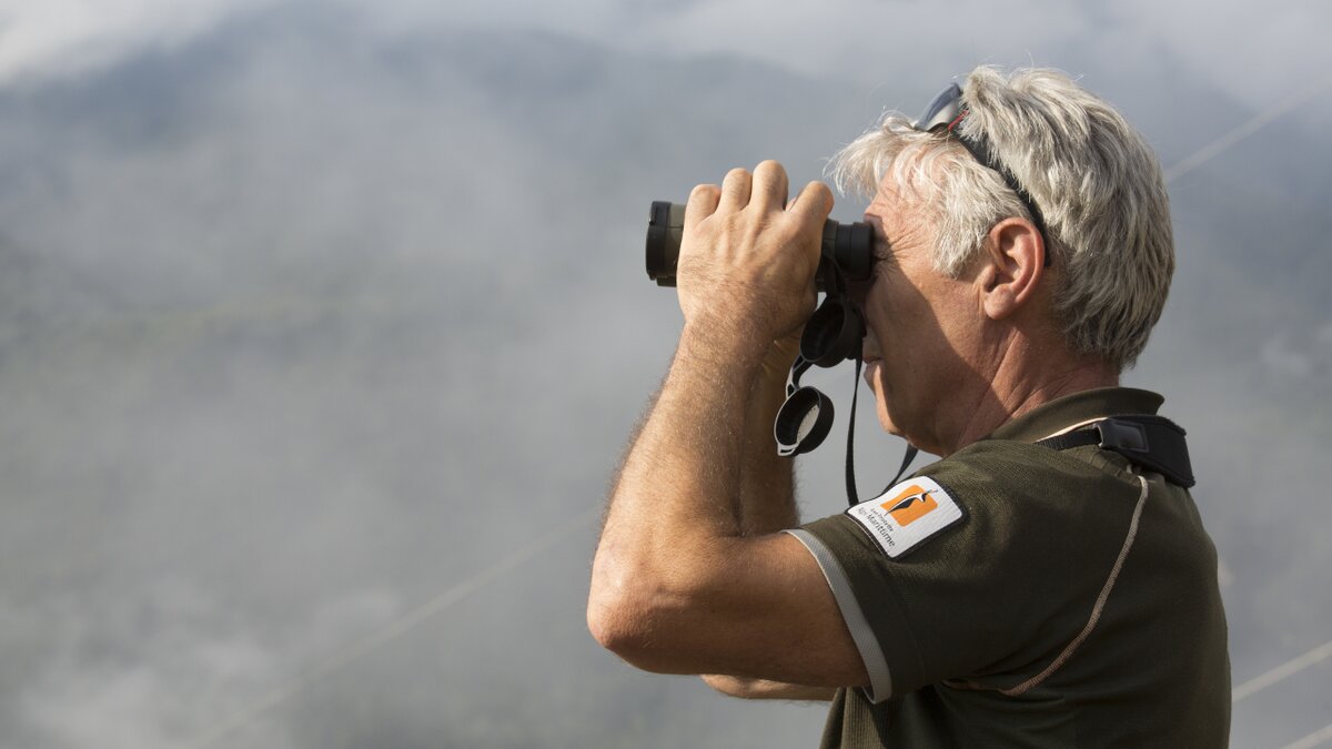 Lo scatto di G. Bernardi mostra un guardiaparco che osserva il cielo con il binocolo. Fine descrizione foto.